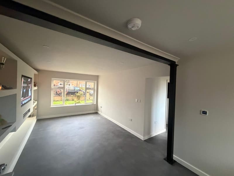 The finished lounge with smooth white walls, a black steel beam, painted media wall and grey floor