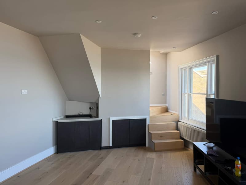 Open-plan kitchen with dark units, pale walls and an oak floor