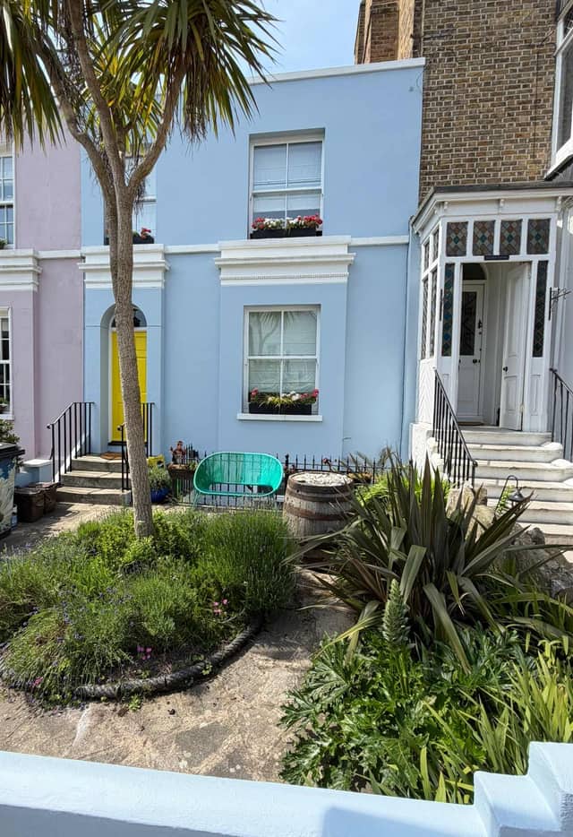 A Georgian terrace painted powder blue with a bright yellow front door, palm trees and a front garden